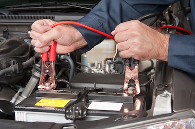 auto mechanic attaching jumper cables to car battery