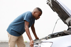 man leaning over car engine due to car troubles